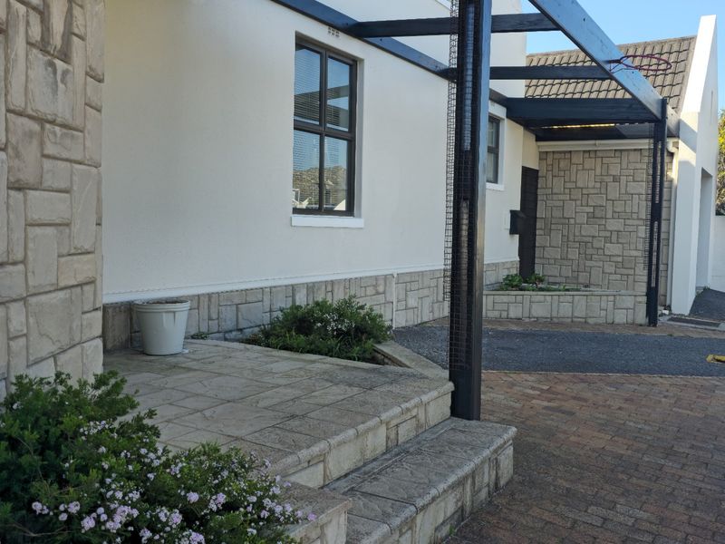 Front exterior view of the property featuring stone cladding, a timber pergola, and a paved driveway with stone steps leading to the entrance.