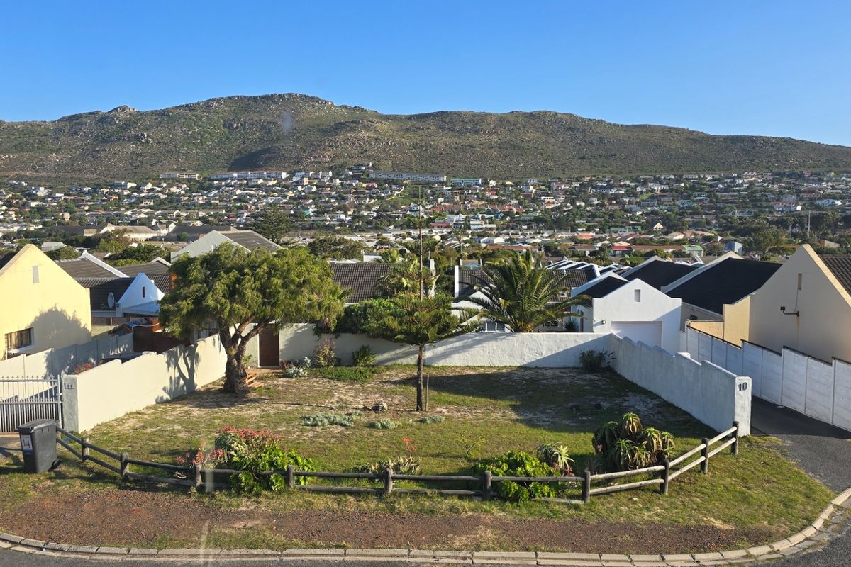 An elevated view of a residential plot featuring a boundary wall, timber fencing, and a paved driveway, set against a mountain backdrop.