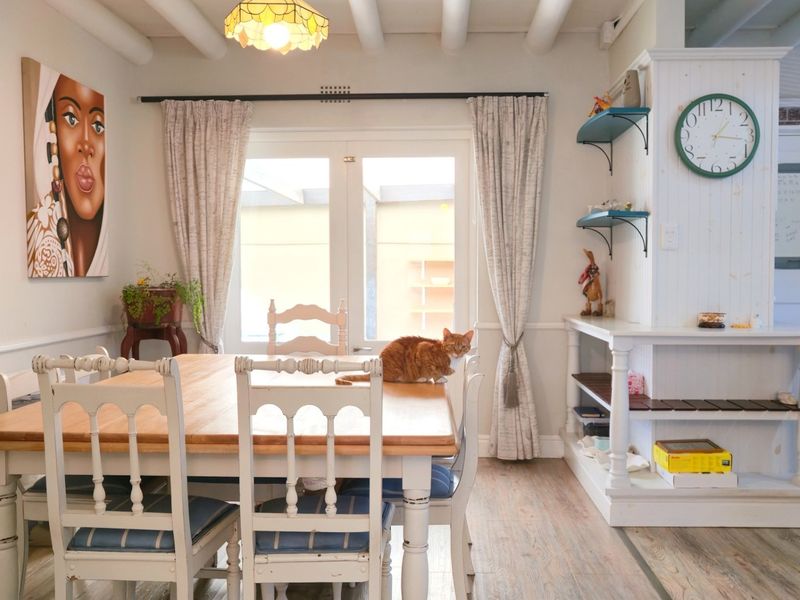 A bright dining room featuring exposed ceiling beams, wainscoting, and a built-in shelving unit, with direct access to the patio through french doors.