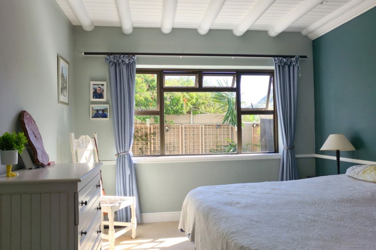 A well-maintained bedroom featuring an exposed beam ceiling, neutral wall tones, and a large window overlooking the rear garden area.