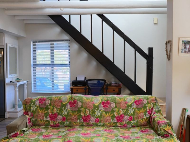 A living area featuring exposed ceiling beams, a staircase with a dark balustrade, and a window with blinds, providing a functional and characterful space.