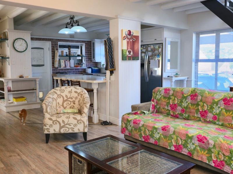 Open plan living and kitchen area featuring exposed beam ceilings, a brick feature wall, breakfast bar, and staircase access.