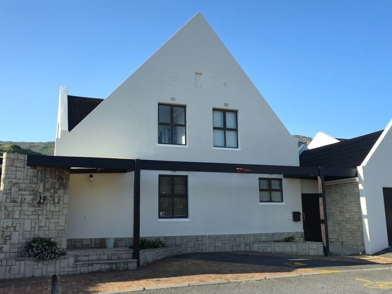 Front elevation of a modern house featuring stone cladding, a pitched roof, paved driveway, and a covered entrance area.