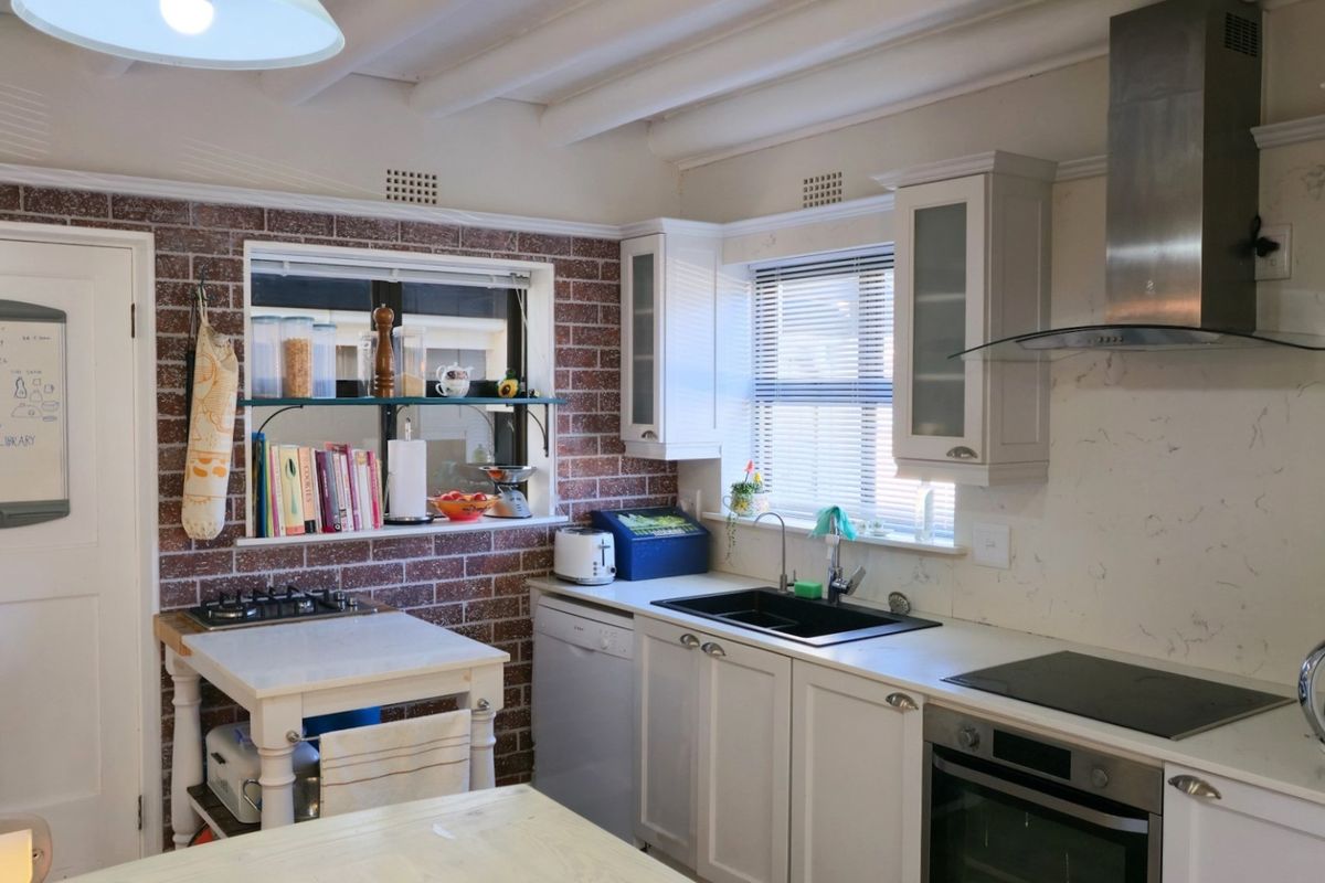 A well-appointed kitchen featuring exposed brick walls, white cabinetry, exposed ceiling beams, and a combination of gas and electric cooking appliances.