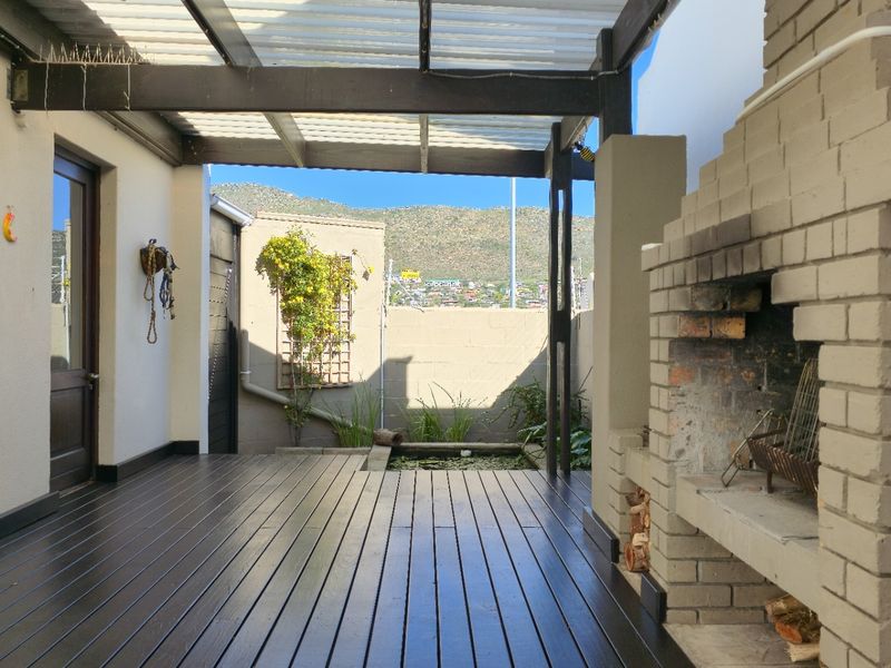 Covered outdoor patio featuring timber decking, a built-in brick braai, and a small water feature, offering a functional space for outdoor entertaining.