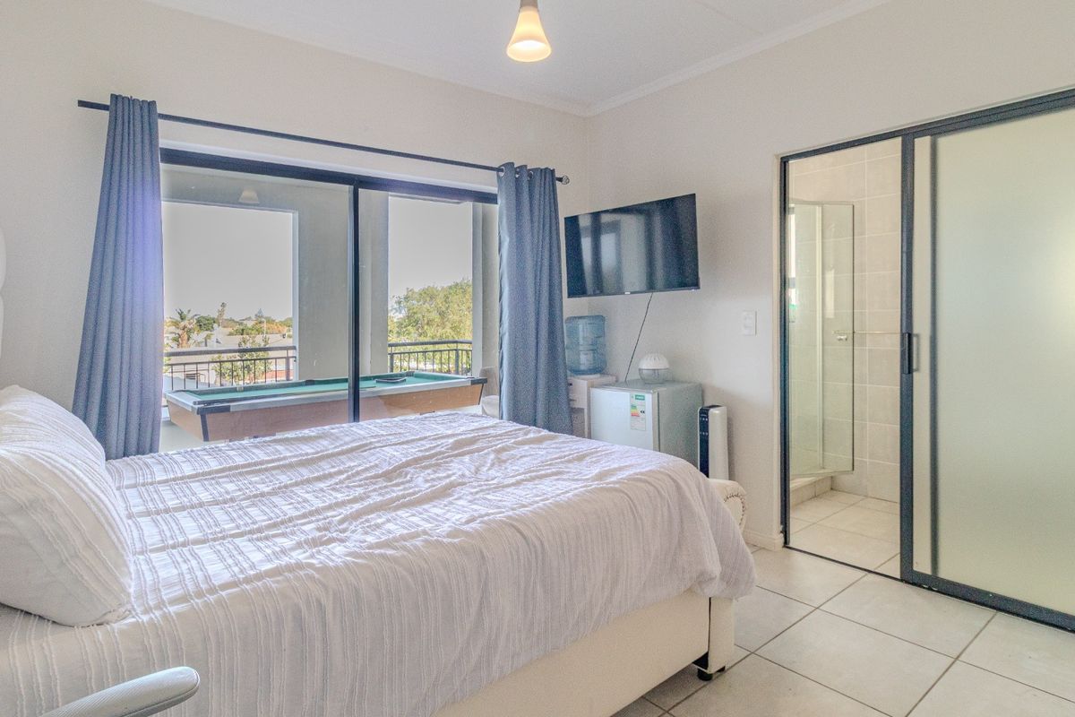 A well-lit bedroom featuring tiled flooring, an en-suite bathroom with a frosted glass door, and direct access to a private balcony.