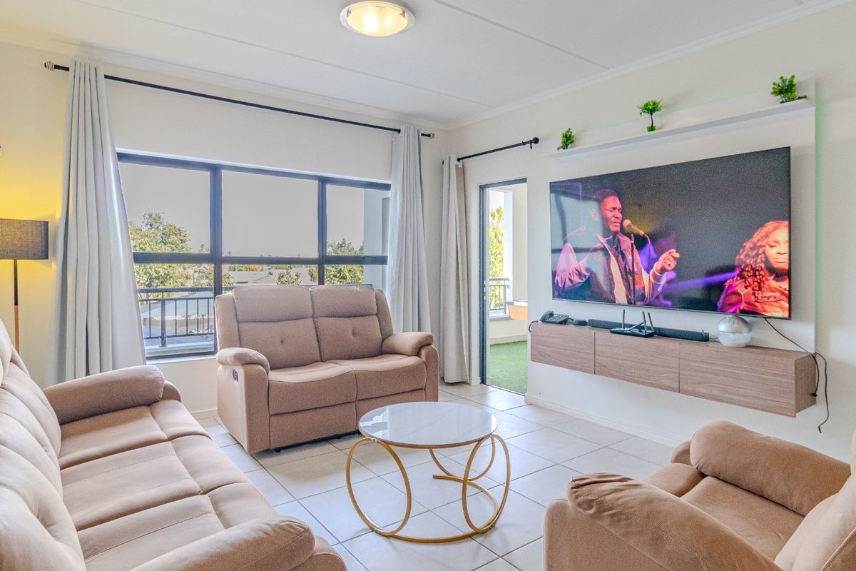 A bright and well-maintained living room featuring tiled flooring, a floating media console, and large windows providing natural light and access to a balcony.