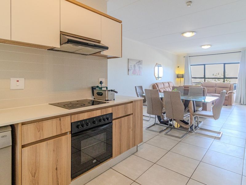 Open-plan living area featuring a modern kitchen with wood-finish cabinetry, electric hob, and oven, flowing into a bright dining and lounge space.