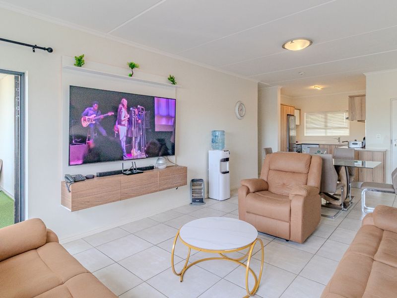 Spacious open-plan living and dining area featuring tiled floors, a modern floating media console, and seamless flow to an adjoining balcony.