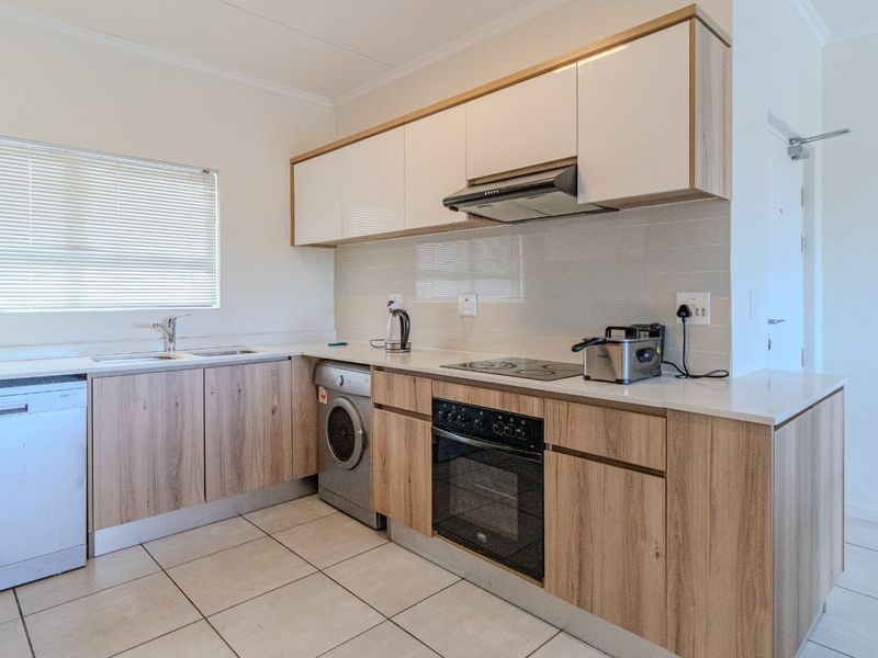 Modern kitchen featuring light wood-grain cabinetry, stone-look countertops, integrated appliances, and neutral tiled flooring in a clean, functional layout.