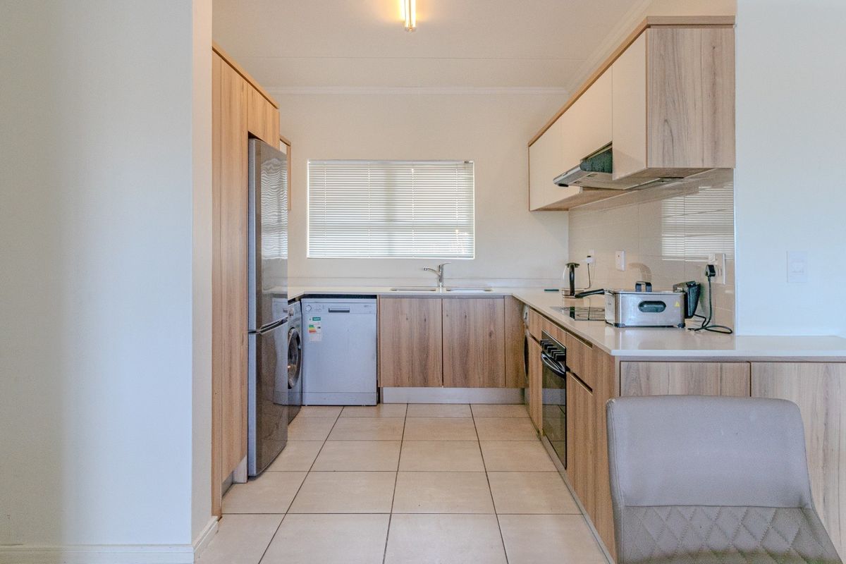 A modern, well-maintained kitchen featuring light wood-finish cabinetry, stone-look countertops, tiled flooring, and integrated appliance spaces.