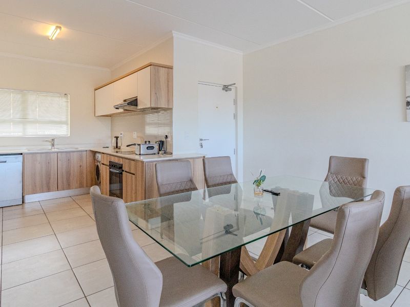 Open-plan living and dining area featuring a modern kitchen with built-in cabinetry, integrated appliances, and neutral tiled flooring throughout.
