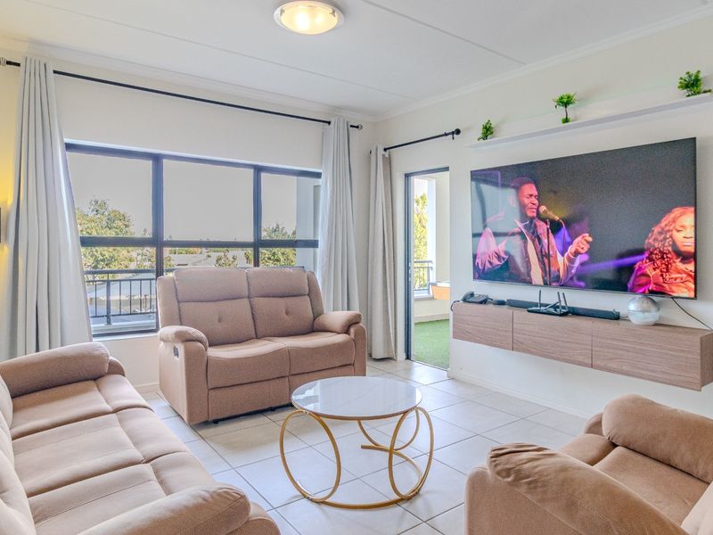 A bright and well-maintained living room featuring tiled flooring, a floating media console, and large windows providing natural light and access to a balcony.