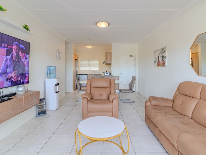 An open-plan living and dining area featuring neutral tiled flooring, a built-in media console, and a functional kitchen space in the background.