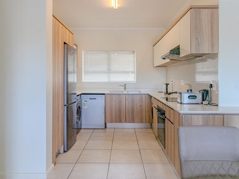A modern, well-maintained kitchen featuring light wood-finish cabinetry, stone-look countertops, tiled flooring, and integrated appliance spaces.
