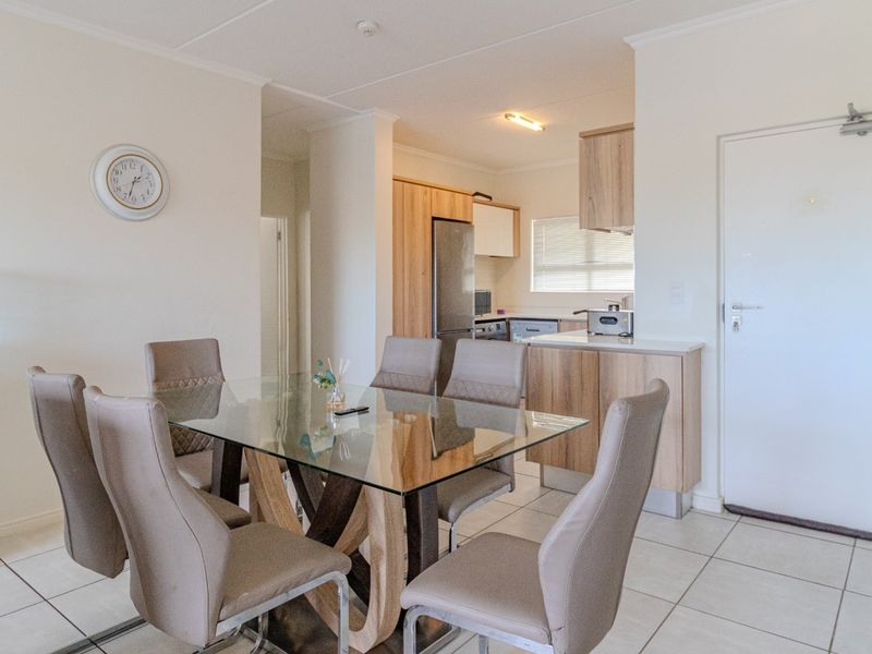 Open-plan dining area seamlessly connected to a functional kitchen featuring light wood cabinetry and tiled flooring throughout.
