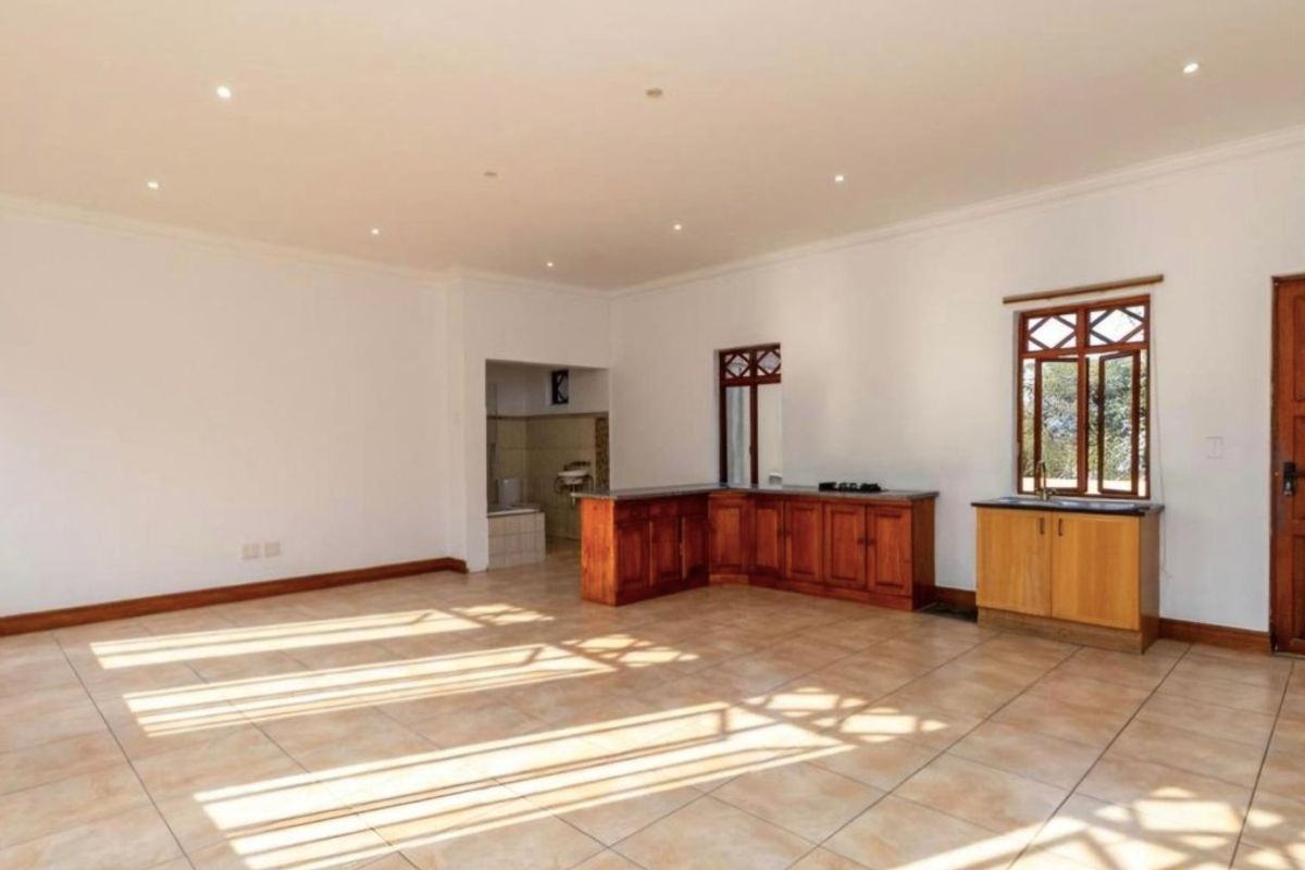 Spacious open-plan living area featuring tiled flooring, recessed lighting, and a functional kitchenette with wooden cabinetry and stone countertops.