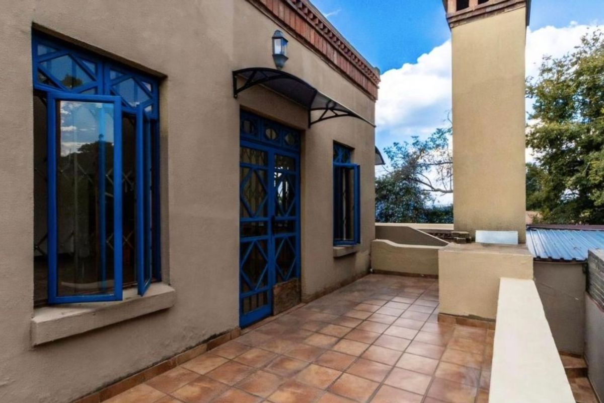 A spacious outdoor balcony featuring tiled flooring, a built-in chimney stack, and distinctive blue metal security doors and window frames.