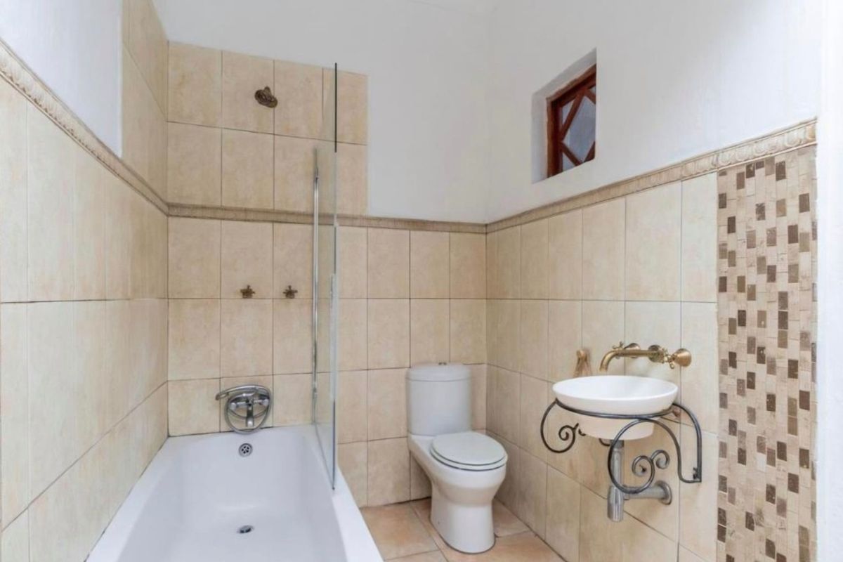 A functional bathroom featuring a bathtub with a glass screen, a wall-mounted basin, and neutral tiled finishes throughout.