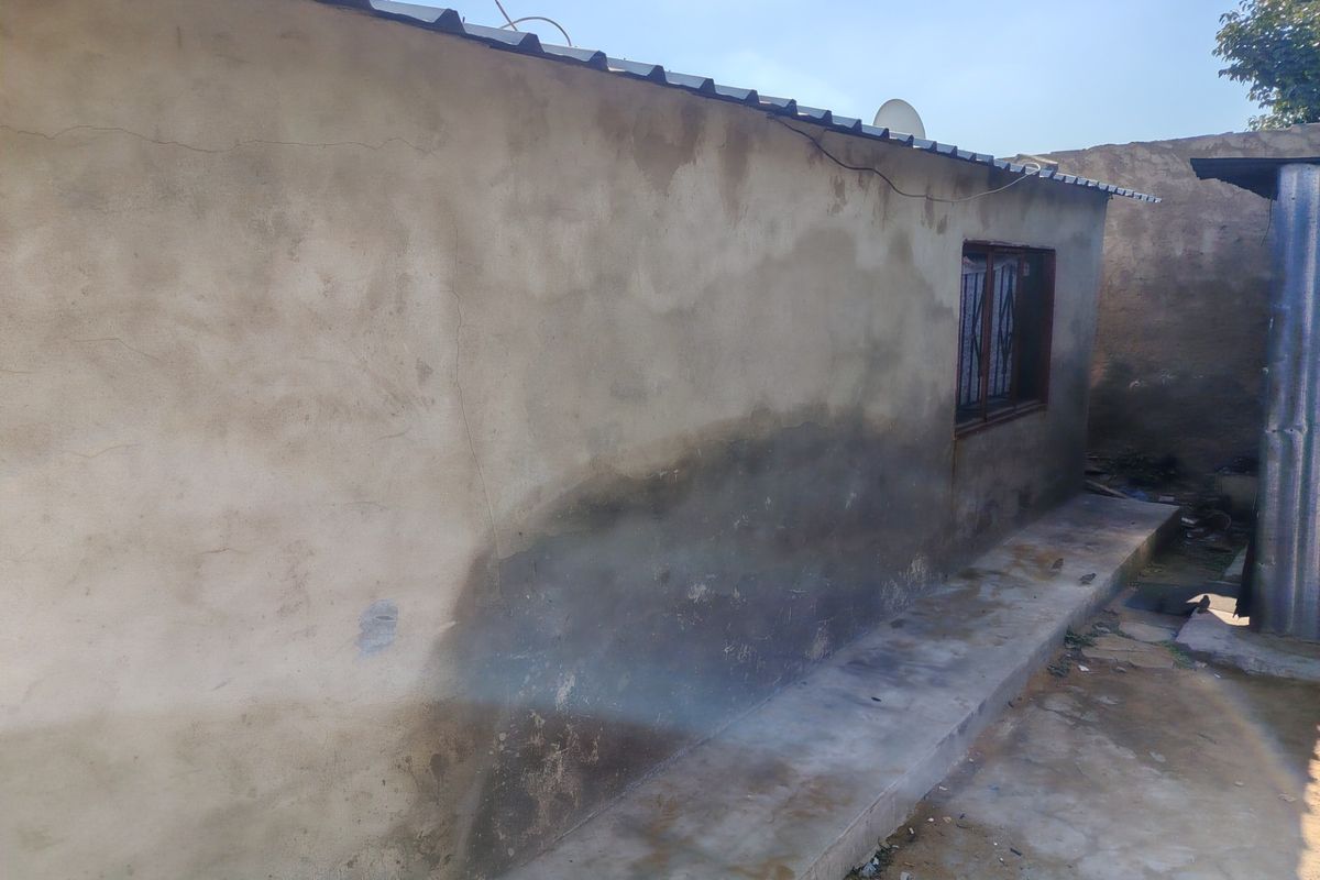 Rear exterior view of the property showing a concrete apron and a wall with visible damp staining and plaster cracking.