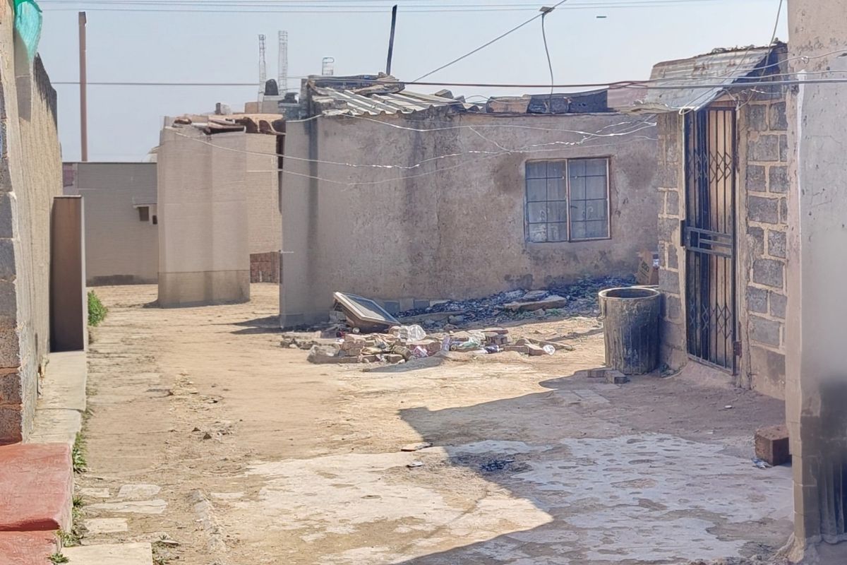 Rear exterior view of a property showing weathered concrete block walls, a security gate, and a damaged roof structure in need of significant maintenance.