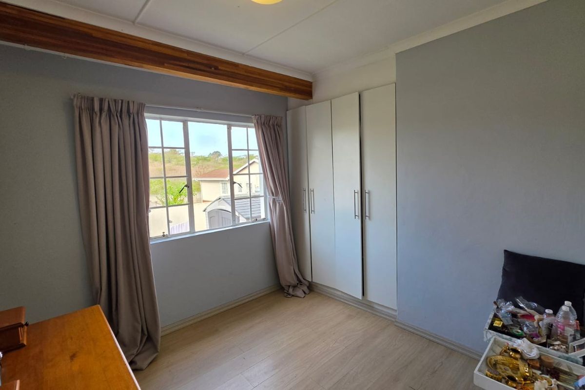 A well-lit bedroom featuring laminate flooring, built-in cupboards, and a decorative timber ceiling beam, offering a clean and functional living space.