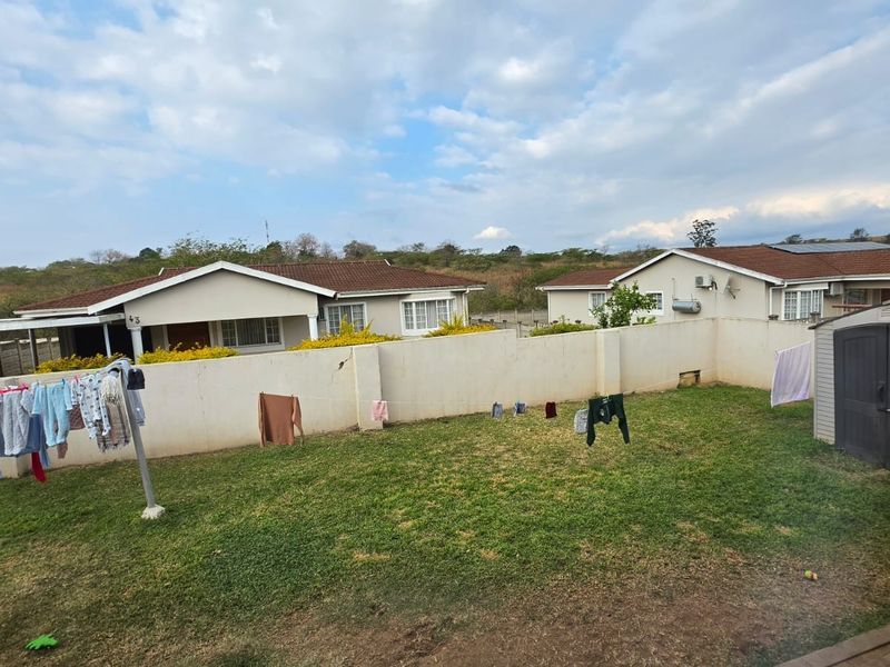 A view of the rear garden area featuring a lawn and perimeter boundary wall, with neighbouring residential properties visible in the background.
