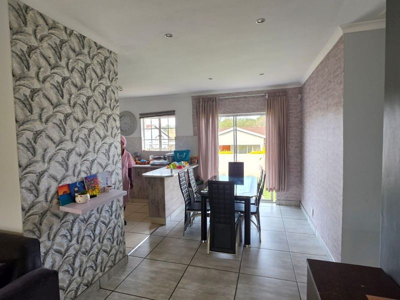 Open-plan living and dining area featuring tiled flooring, recessed lighting, and a breakfast bar connecting to the kitchen, with access to the rear exterior.
