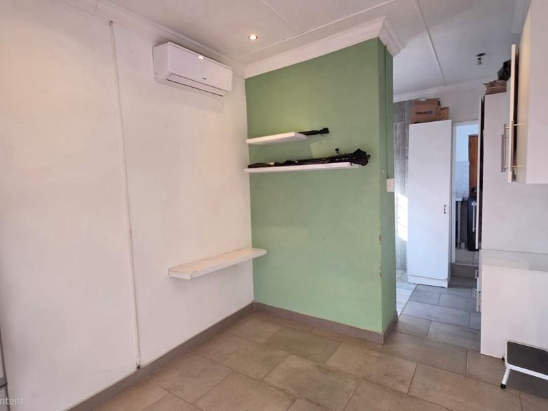 A functional kitchen area featuring tiled flooring, built-in shelving, and a wall-mounted air conditioning unit, leading into a secondary utility or pantry space.