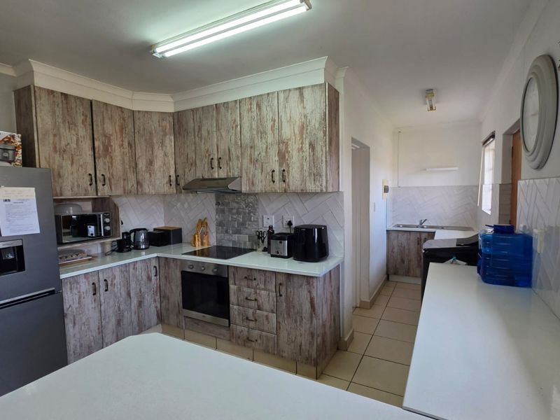 A functional kitchen featuring wood-look cabinetry, a built-in oven and hob, tiled backsplash, and an adjoining scullery area with a double sink.