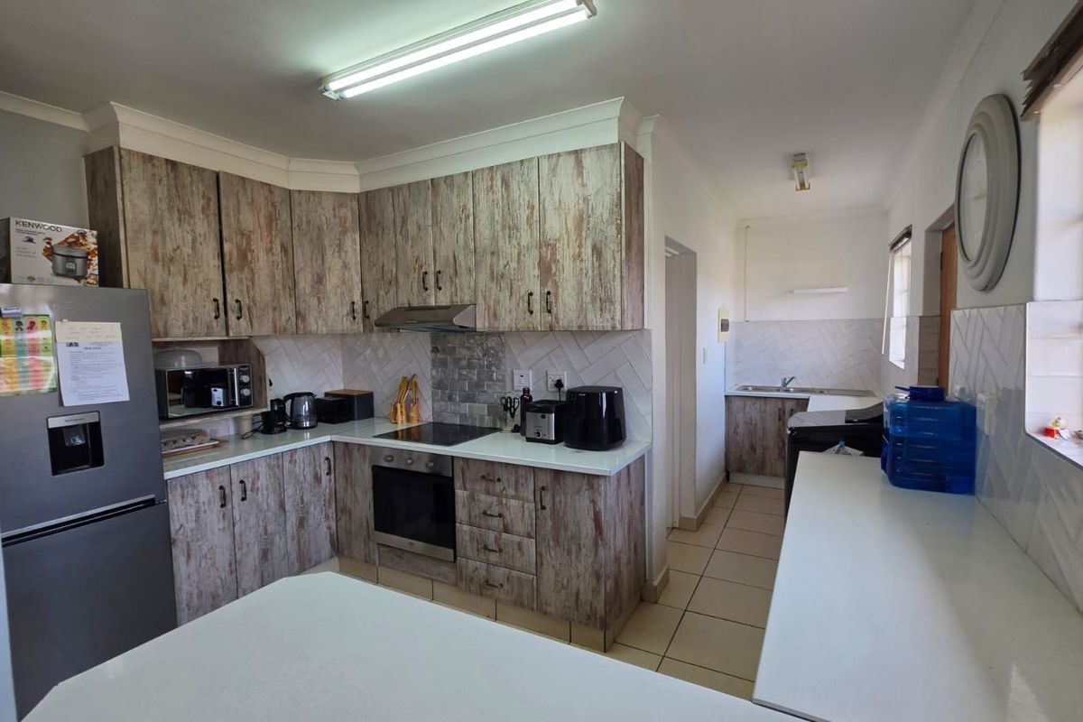 A functional kitchen featuring wood-look cabinetry, a built-in oven and hob, tiled backsplash, and an adjoining scullery area with a double sink.