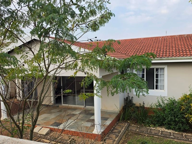 Rear view of the house featuring a covered tiled patio, sliding glass doors, and a terracotta tiled roof set within a landscaped garden.