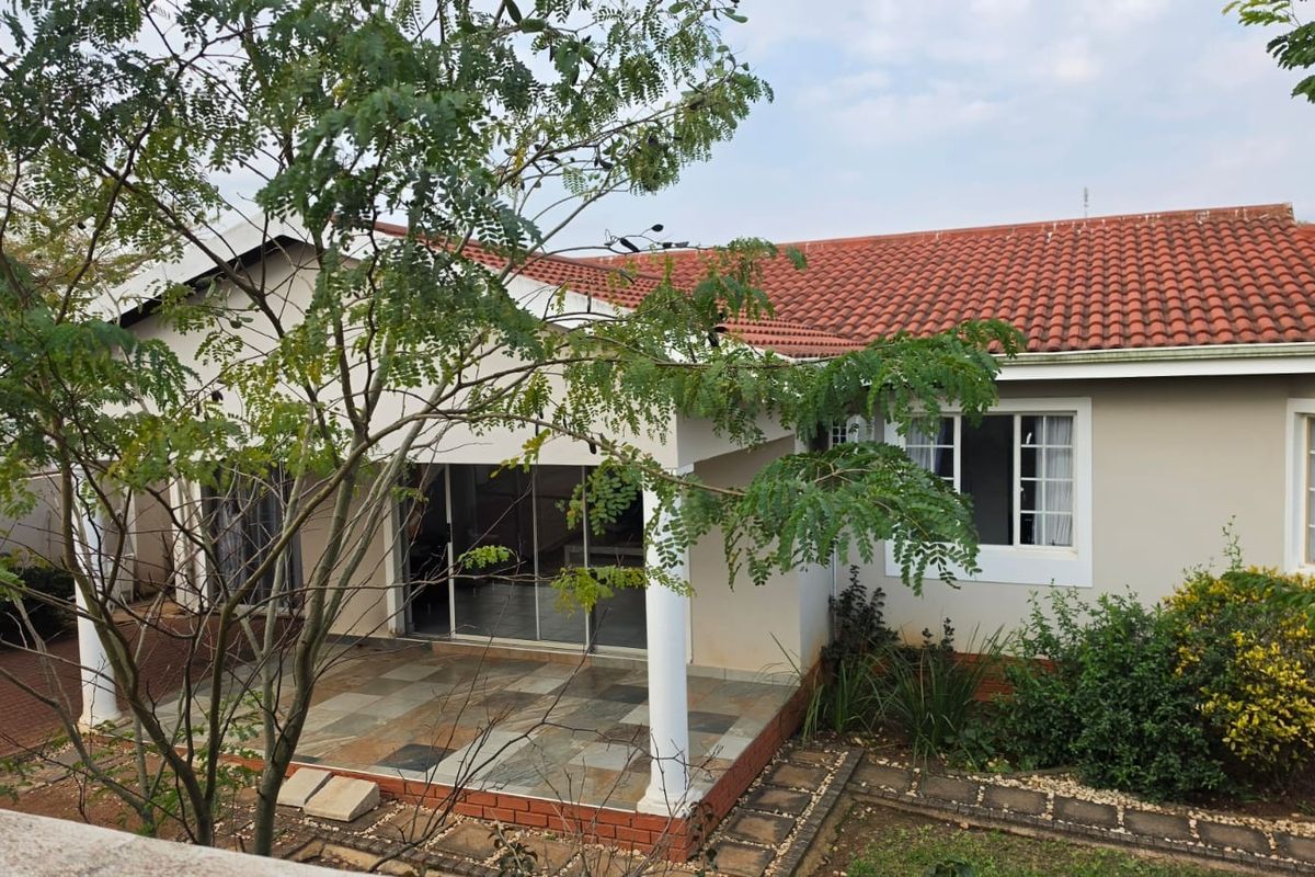 Rear view of the house featuring a covered tiled patio, sliding glass doors, and a terracotta tiled roof set within a landscaped garden.