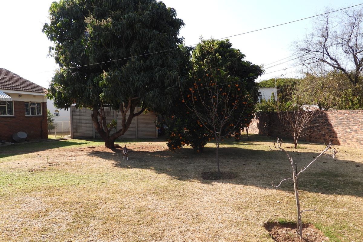 A spacious rear garden featuring mature trees, a brick boundary wall, and a precast concrete fence.