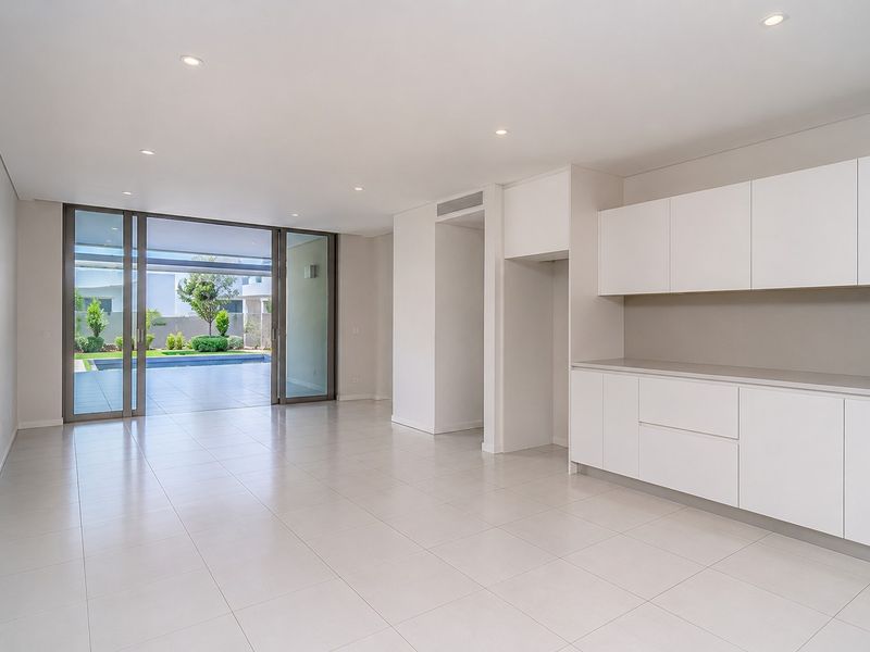 Spacious open-plan living area featuring sleek white cabinetry, tiled floors, and large sliding glass doors opening to a private patio and pool area.