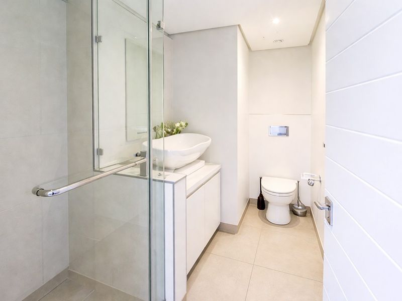 Modern bathroom featuring a glass-enclosed shower, a contemporary vessel sink with vanity storage, and a wall-mounted toilet with neutral floor tiling.