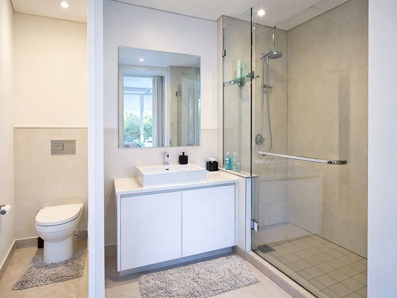 Modern bathroom featuring a wall-mounted toilet, sleek vanity with vessel sink, and a spacious walk-in shower with a glass enclosure.
