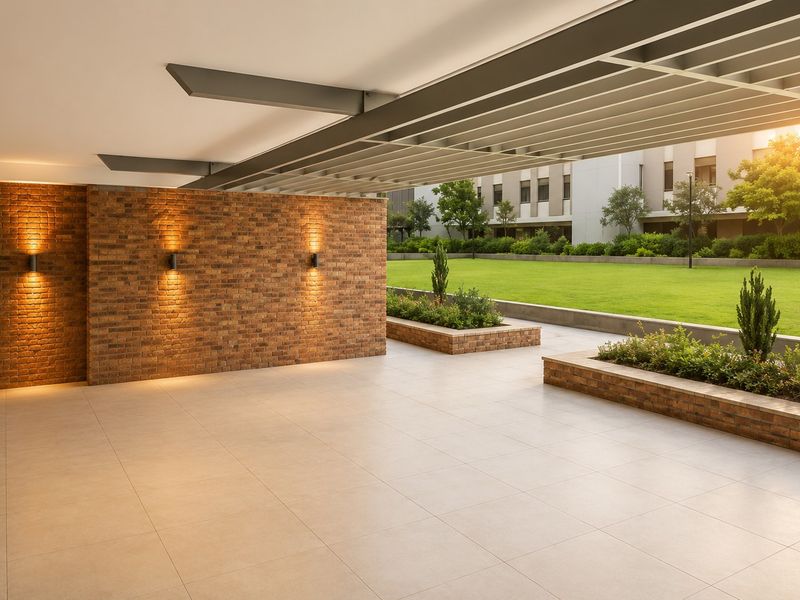A spacious, modern covered patio featuring tiled flooring, exposed brick walls with accent lighting, and built-in planters overlooking a landscaped garden area.