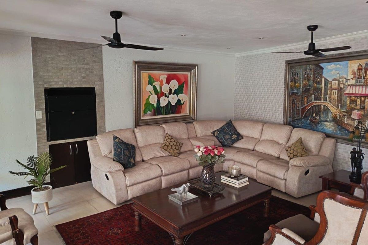 A comfortable living room featuring a built-in fireplace, dual ceiling fans, and decorative textured wallpaper, creating a warm and inviting atmosphere.