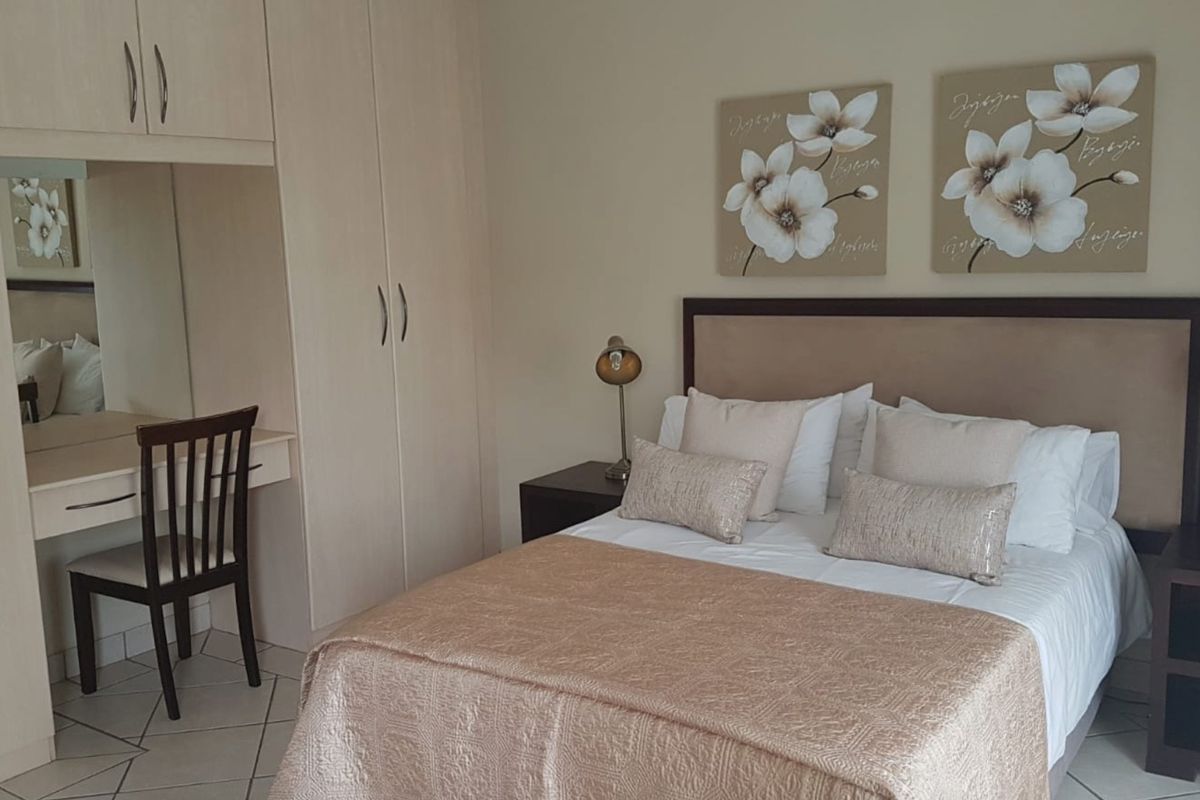 A well-maintained bedroom featuring built-in cupboards, a integrated vanity unit, and neutral tiled flooring.
