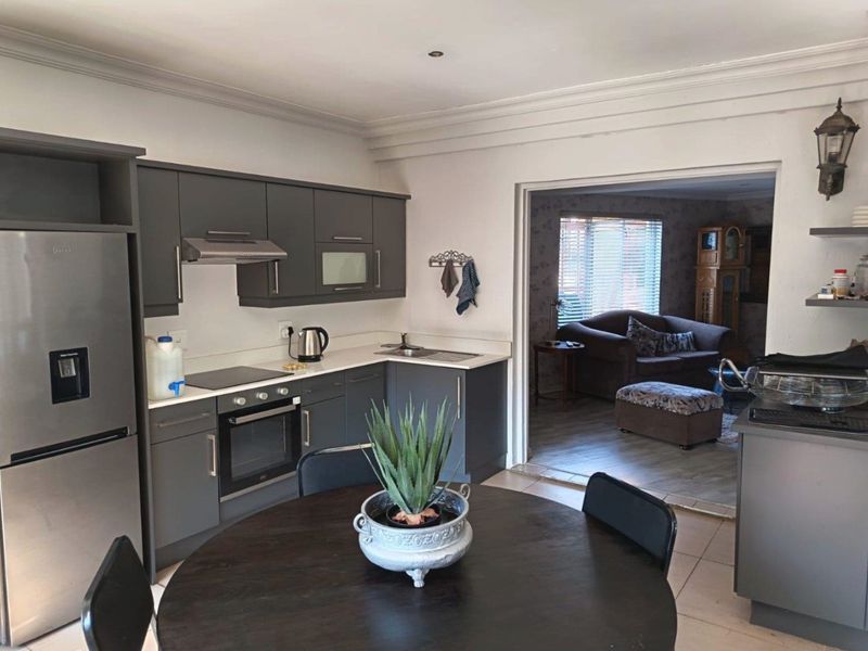 Open-plan kitchen featuring modern grey cabinetry, integrated appliances, and tiled flooring, flowing into an adjacent living area.