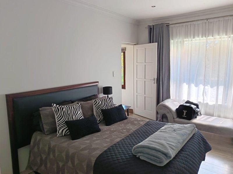 A well-maintained bedroom featuring neutral walls, laminate flooring, recessed lighting, and direct access to a window with curtain treatments.