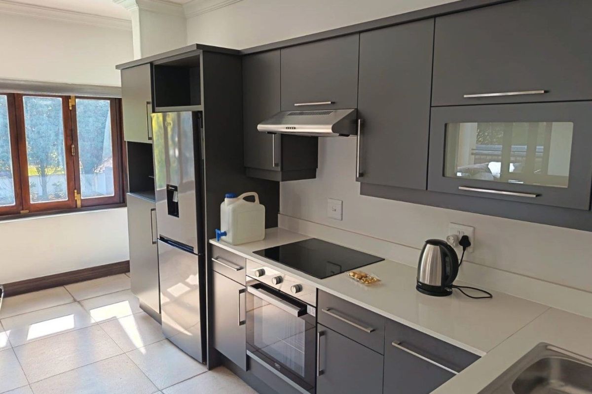 Modern kitchen featuring dark grey cabinetry, stone countertops, integrated electric hob, oven, and extractor fan with tiled flooring and natural light.