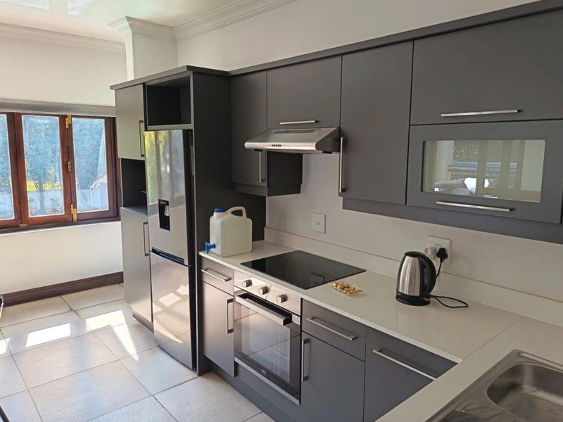 Modern kitchen featuring dark grey cabinetry, stone countertops, integrated electric hob, oven, and extractor fan with tiled flooring and natural light.