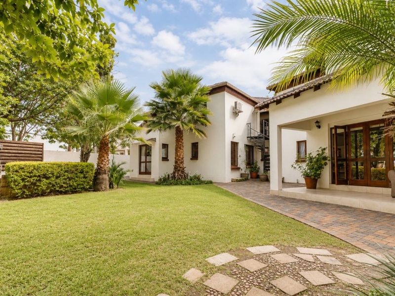 A well-maintained rear garden featuring a lush lawn, covered patio area, stone water feature, and a spiral staircase leading to the upper level.