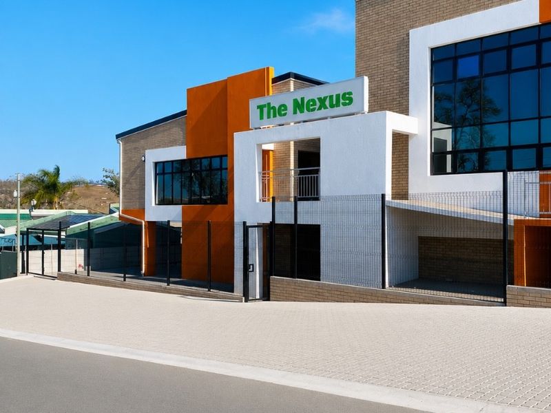 Modern office building exterior featuring a clean brick and orange accent facade with secure perimeter fencing and paved driveway access.