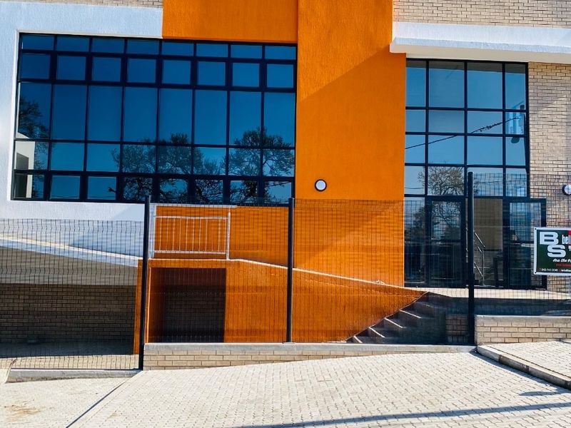 Modern office building exterior featuring a vibrant orange accent wall, large glass windows, paved driveway, and accessible ramp and stair entry.