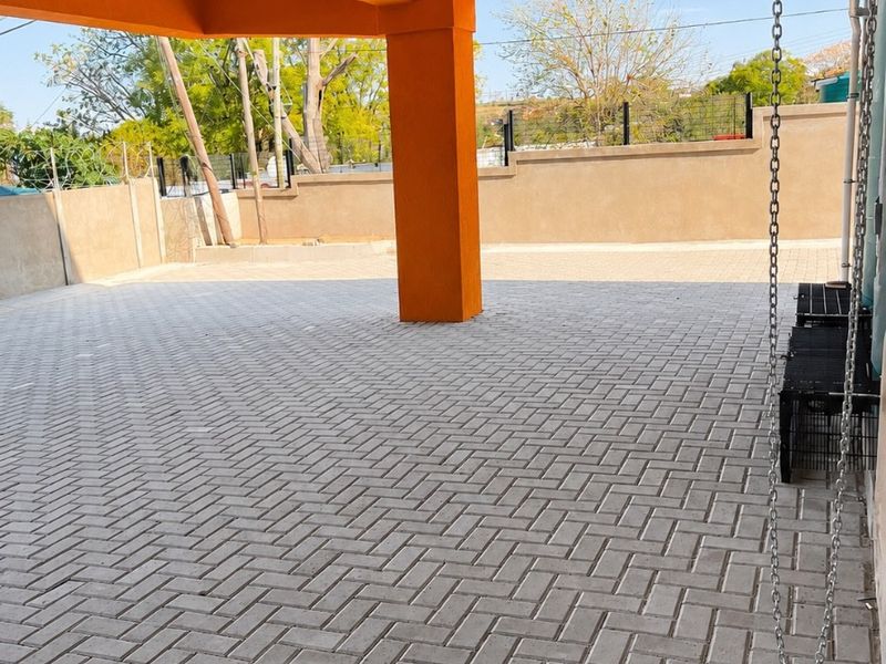 A spacious covered outdoor patio area featuring durable herringbone paving, structural support columns, and a secure perimeter wall.