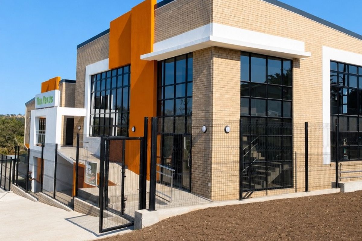 Modern office building exterior featuring brick cladding, large glass windows, and a concrete accessibility ramp with secure perimeter fencing.