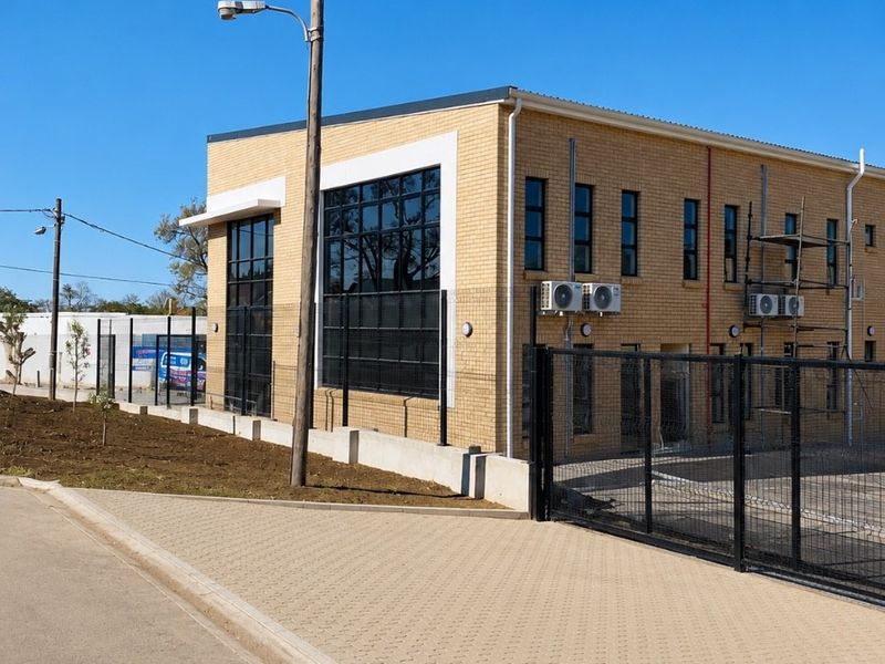 Modern brick office building exterior featuring large windows, secure perimeter fencing, and paved access area.
